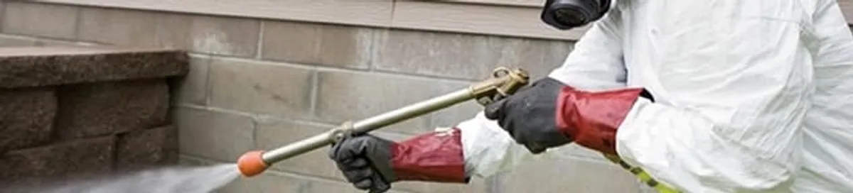 Pest control technician applying exterior insect treatment along a home foundation in Boston, MA