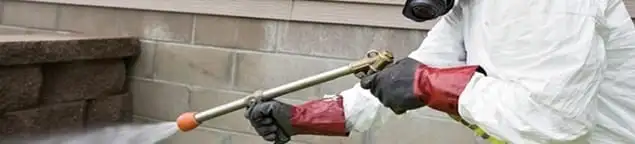 Pest control technician applying exterior insect treatment along a home foundation in Boston, MA
