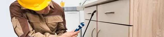 Roach exterminator applying treatment under kitchen cabinets in Boston, MA